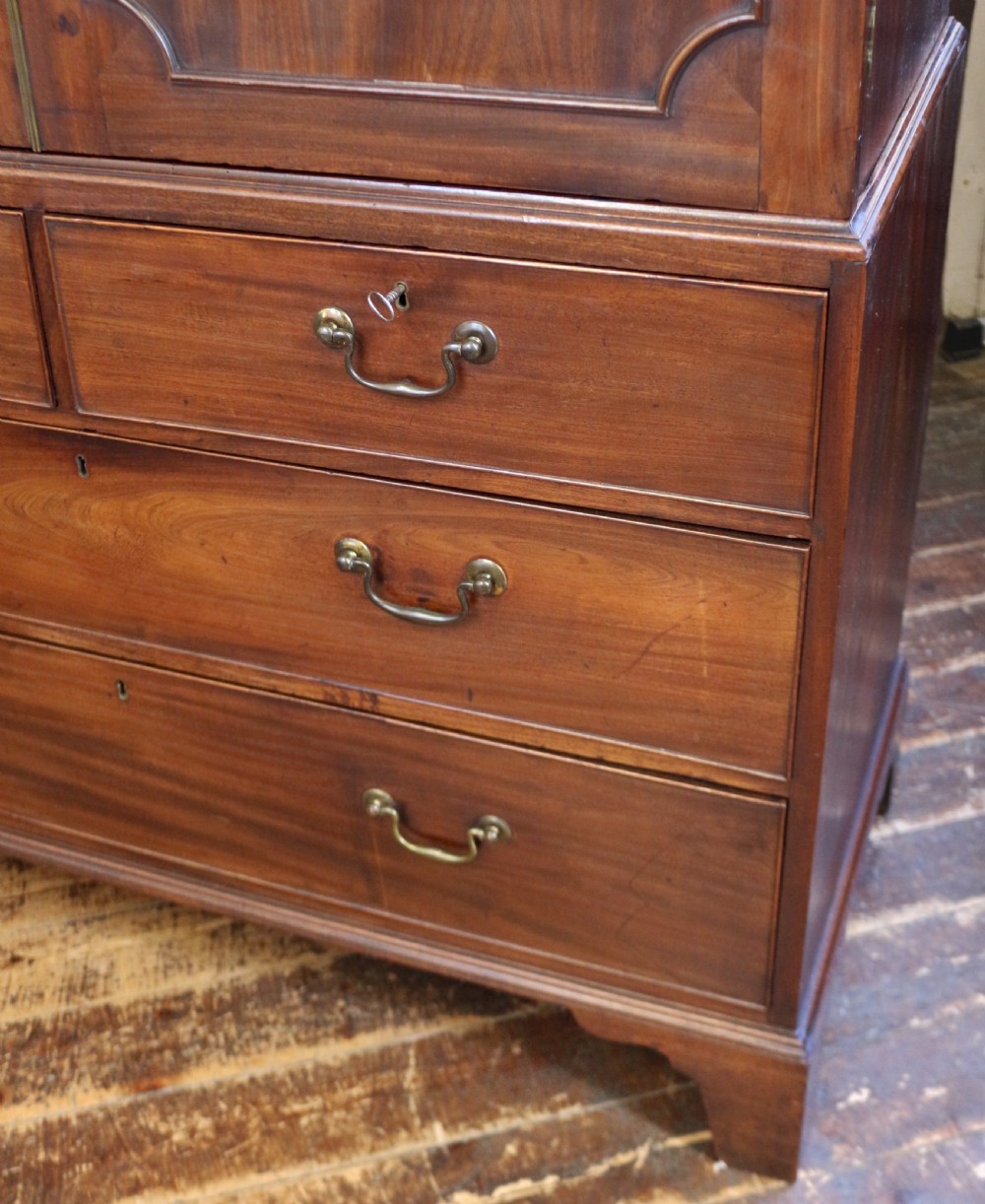 A Georgian mahogany linen press featuring panelled double doors above a chest with two short and two long drawers raised on bracket feet. View X