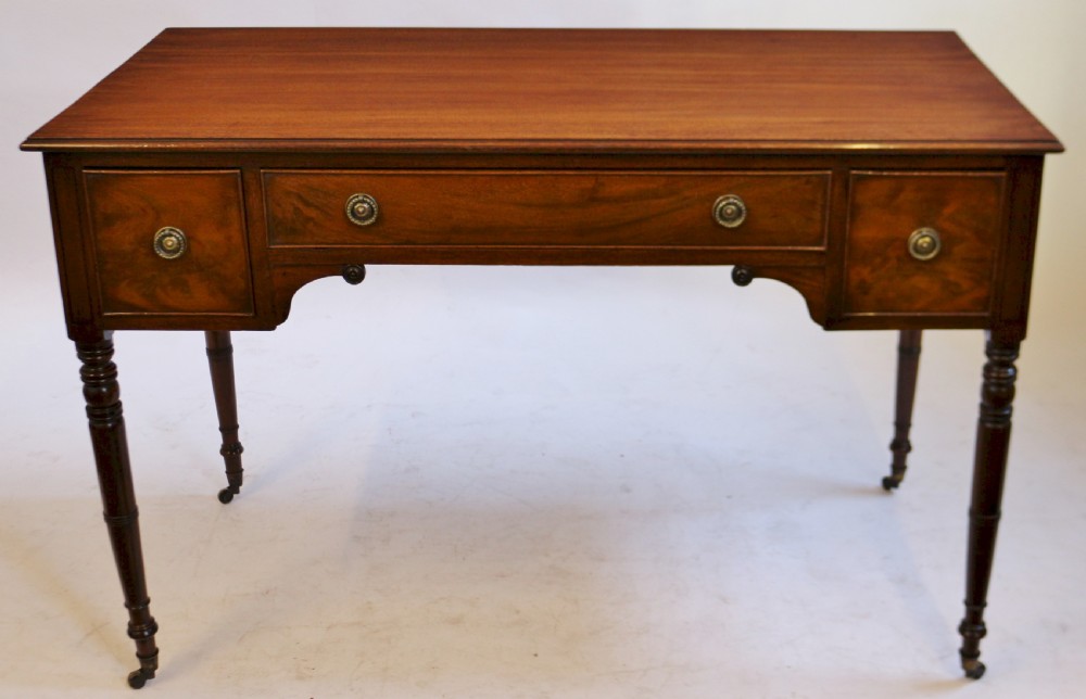 A George IV mahogany kneehole writing table with three drawers, turned legs, brass rosette handles, and brass castors.