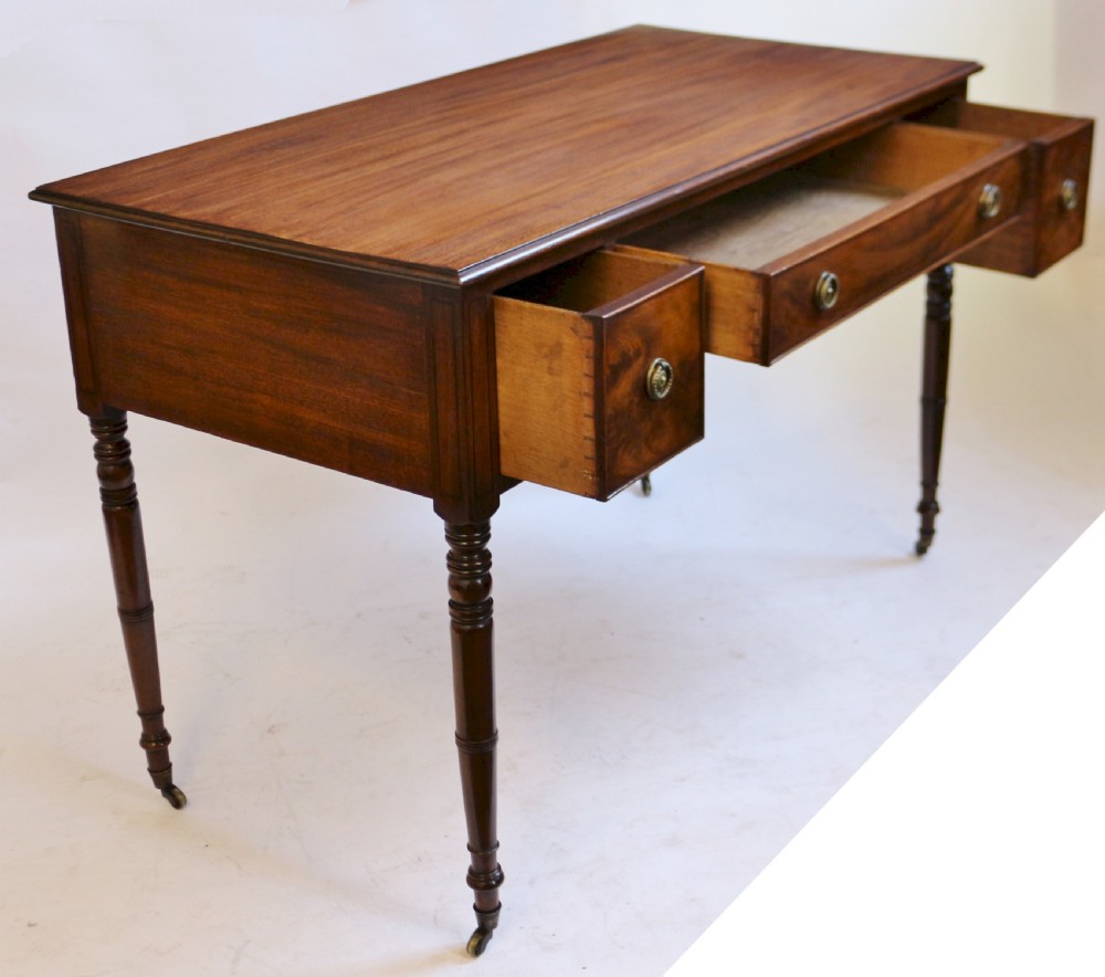 A George IV mahogany kneehole writing table with three drawers, turned legs, brass rosette handles, and brass castors. View II
