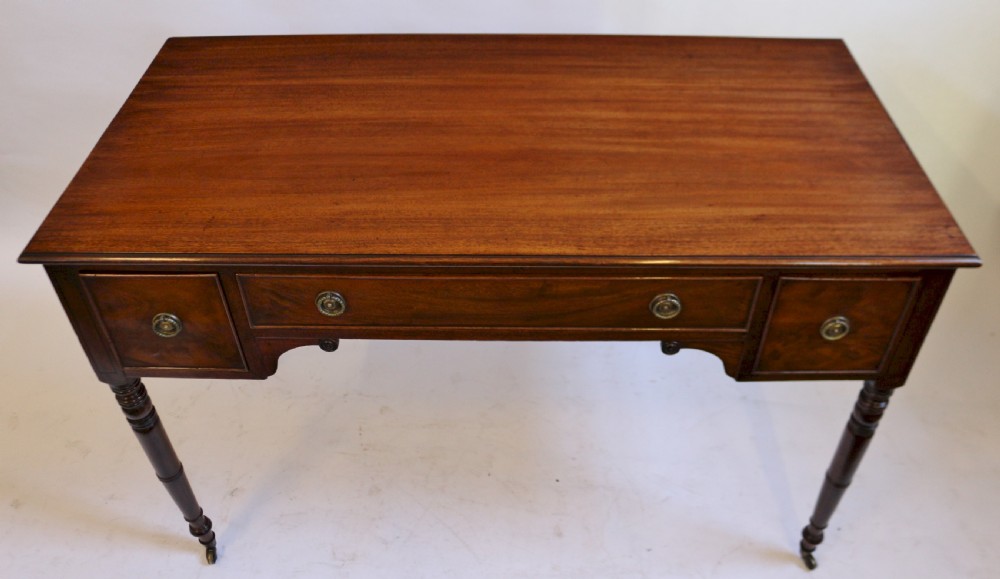 A George IV mahogany kneehole writing table with three drawers, turned legs, brass rosette handles, and brass castors. View IV