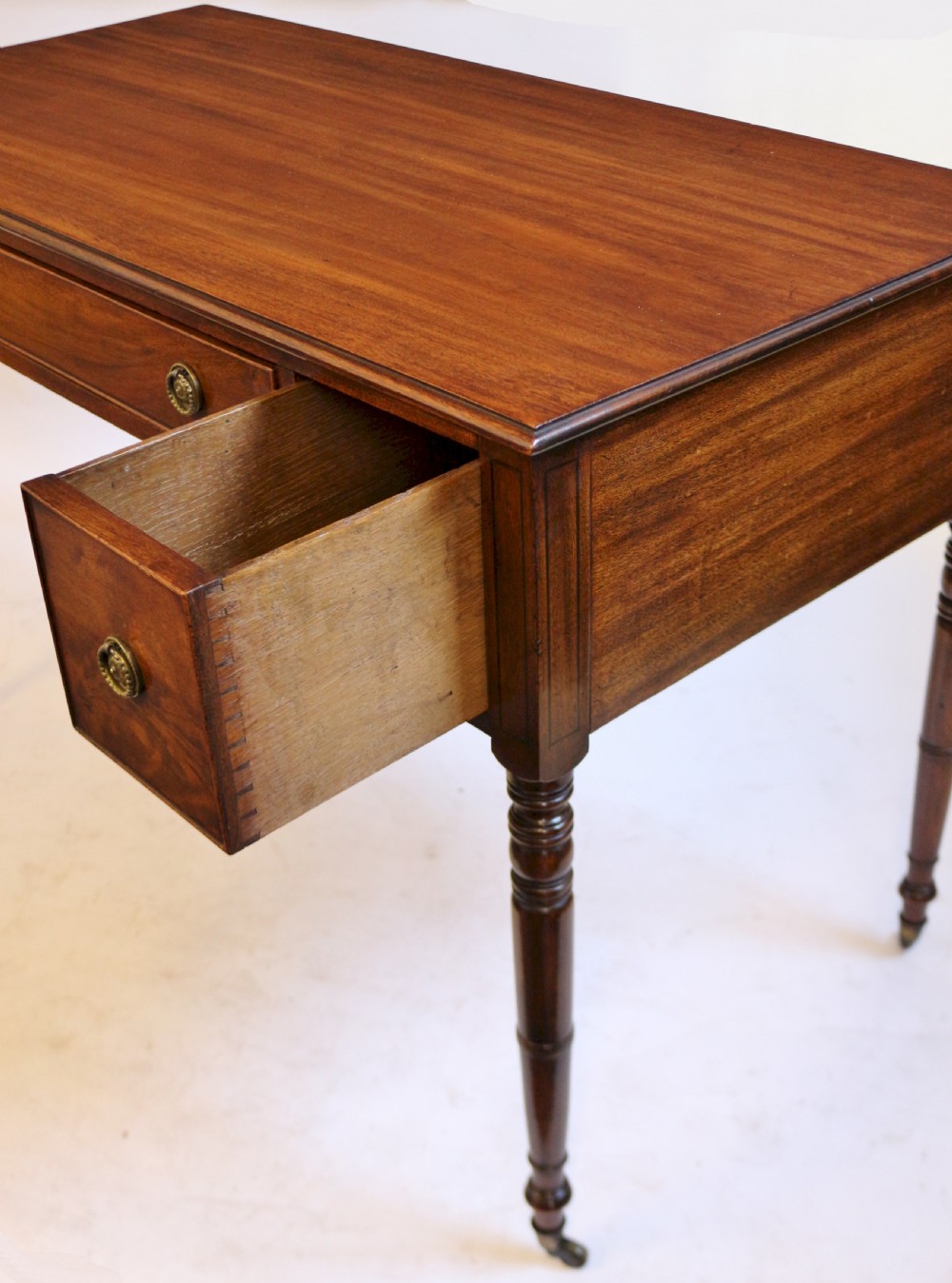 A George IV mahogany kneehole writing table with three drawers, turned legs, brass rosette handles, and brass castors. View V