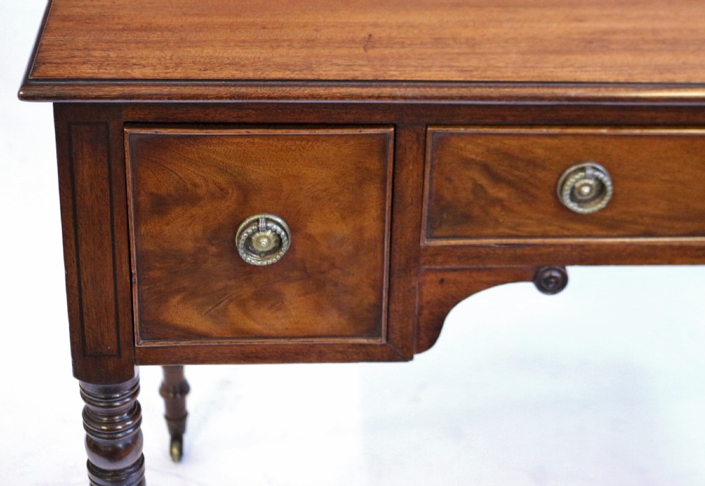 A George IV mahogany kneehole writing table with three drawers, turned legs, brass rosette handles, and brass castors. View VI