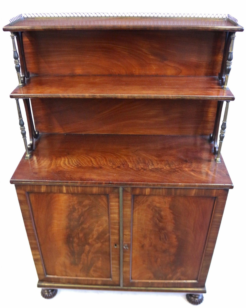 A Regency flame mahogany chiffonier featuring a two-door base cupboard, a two-tier shelf back supported by slender brass pillars, and a pierced brass gallery rail. View II
