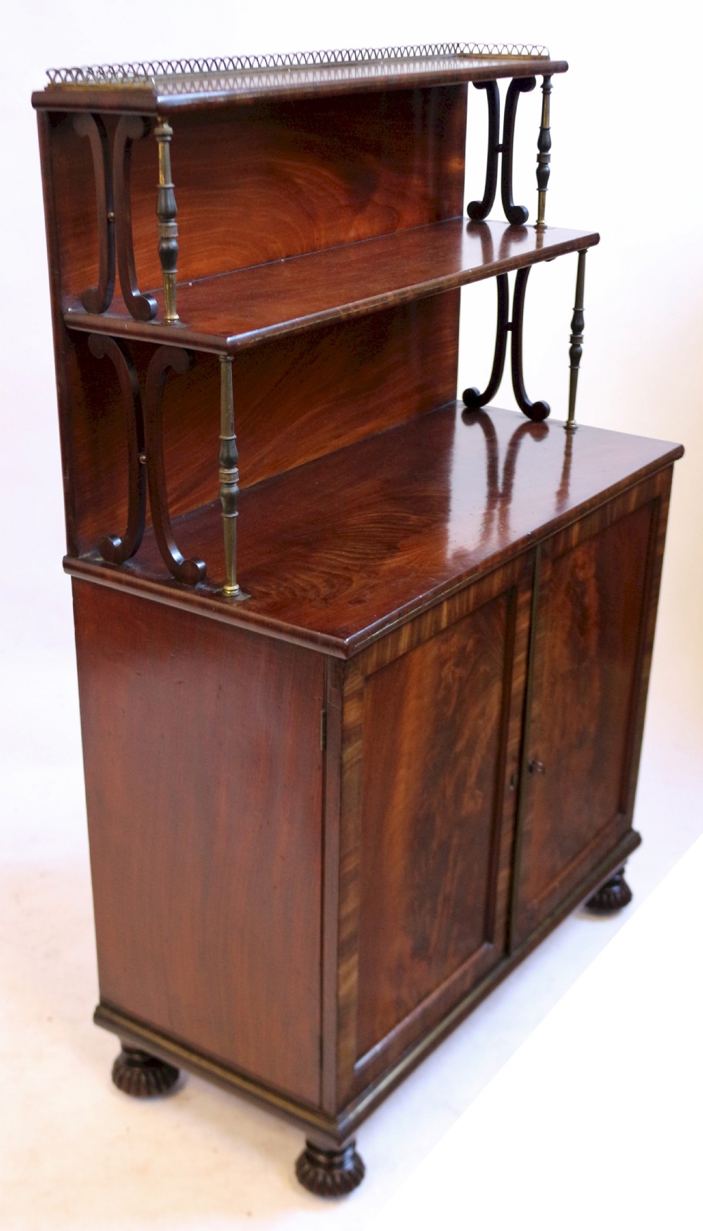 A Regency flame mahogany chiffonier featuring a two-door base cupboard, a two-tier shelf back supported by slender brass pillars, and a pierced brass gallery rail. View V