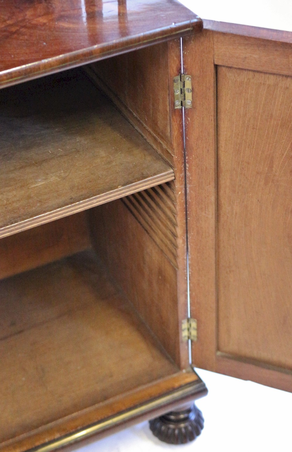 A Regency flame mahogany chiffonier featuring a two-door base cupboard, a two-tier shelf back supported by slender brass pillars, and a pierced brass gallery rail. View VII