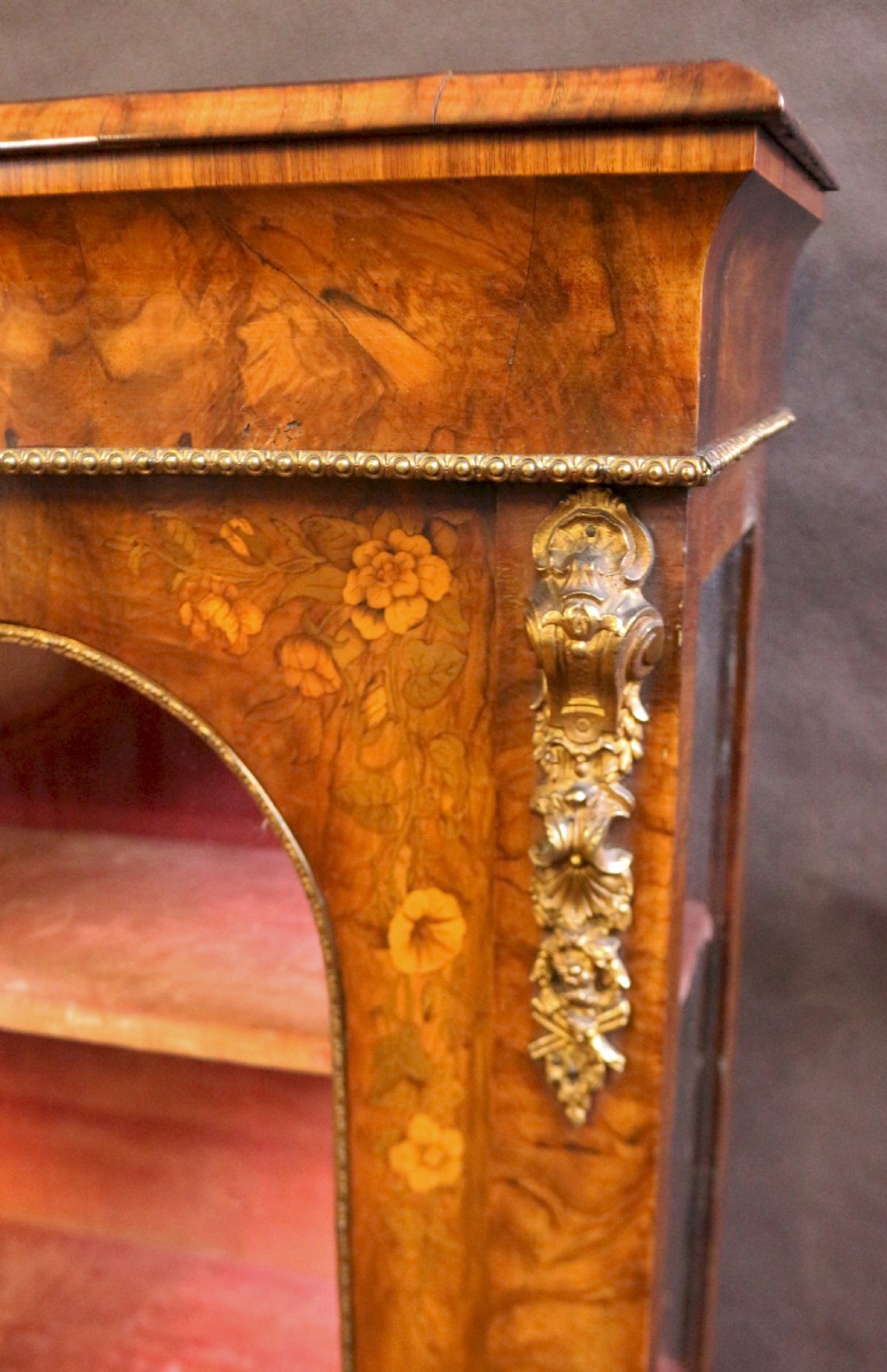 A Victorian burr walnut pier cabinet featuring floral marquetry inlays, gilt ormolu mounts, and double arched glass doors revealing shelves lined in red fabric. View VIII