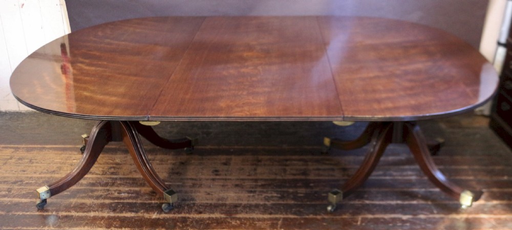 An extending mahogany twin pedestal dining table featuring rounded D-ends, a removable central leaf, reeded splayed legs, and brass castors.