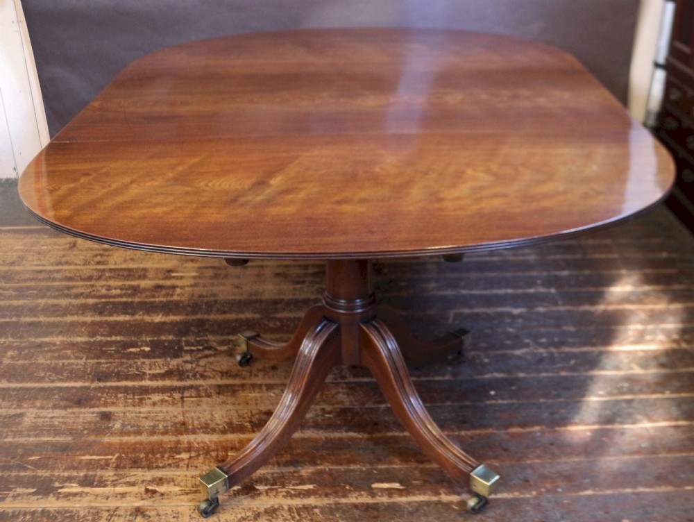 An extending mahogany twin pedestal dining table featuring rounded D-ends, a removable central leaf, reeded splayed legs, and brass castors. View II