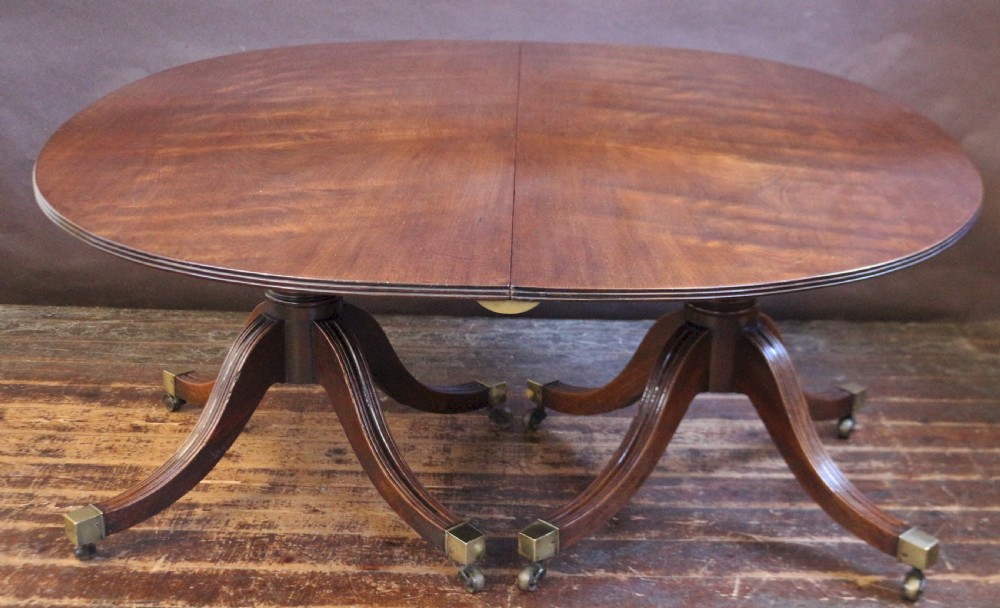 An extending mahogany twin pedestal dining table featuring rounded D-ends, a removable central leaf, reeded splayed legs, and brass castors. View III