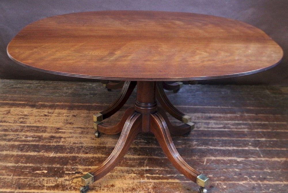 An extending mahogany twin pedestal dining table featuring rounded D-ends, a removable central leaf, reeded splayed legs, and brass castors. View IV