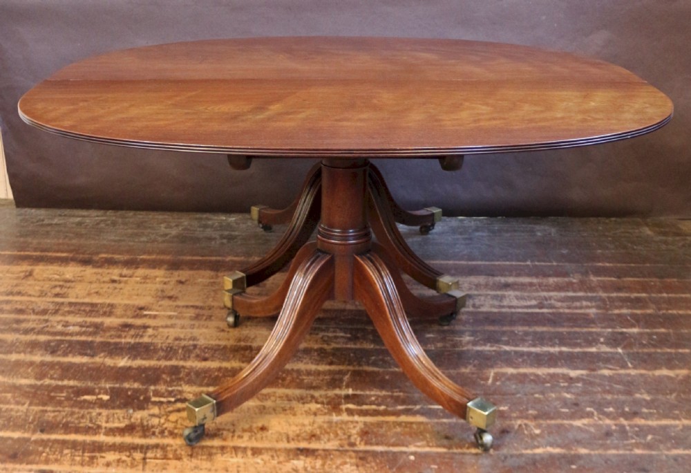 An extending mahogany twin pedestal dining table featuring rounded D-ends, a removable central leaf, reeded splayed legs, and brass castors. View V