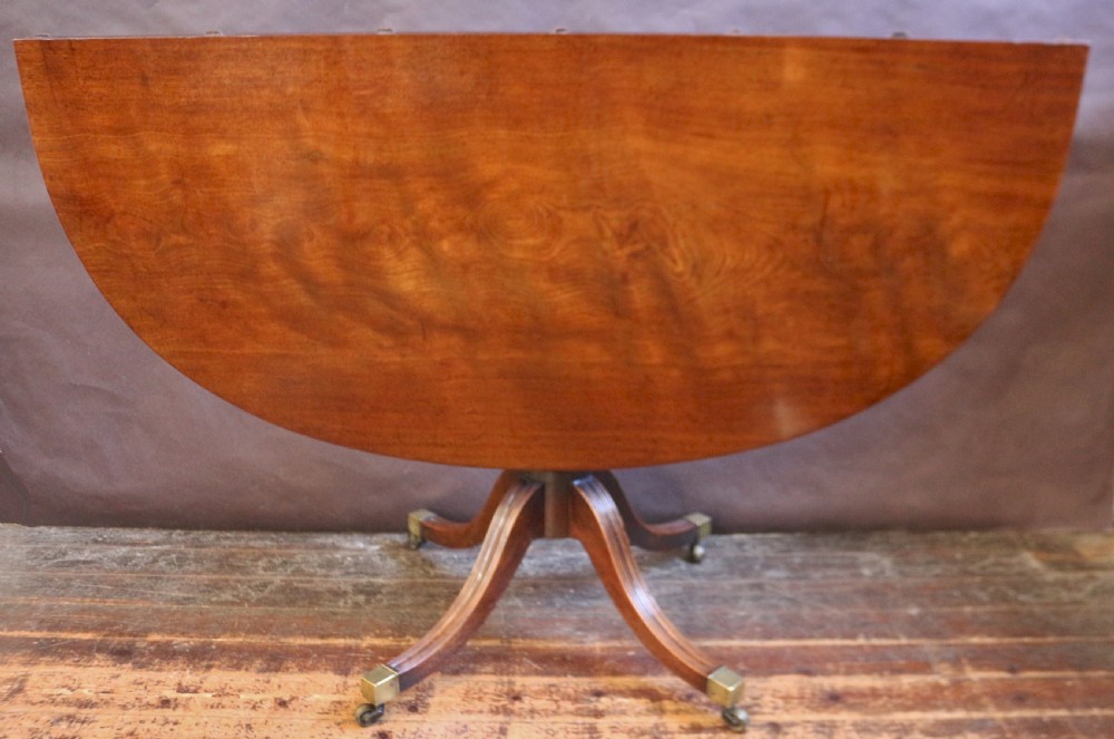 An extending mahogany twin pedestal dining table featuring rounded D-ends, a removable central leaf, reeded splayed legs, and brass castors. View VII
