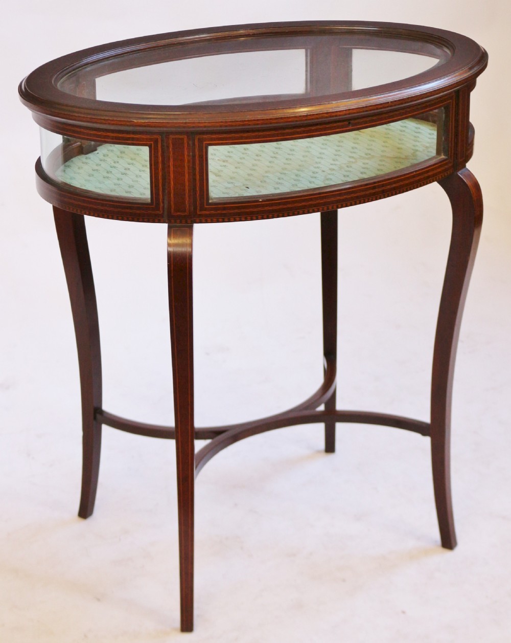 An Edwardian oval mahogany bijouterie table with glass top and sides, satinwood line inlay, curved legs, and an X-form stretcher. View II