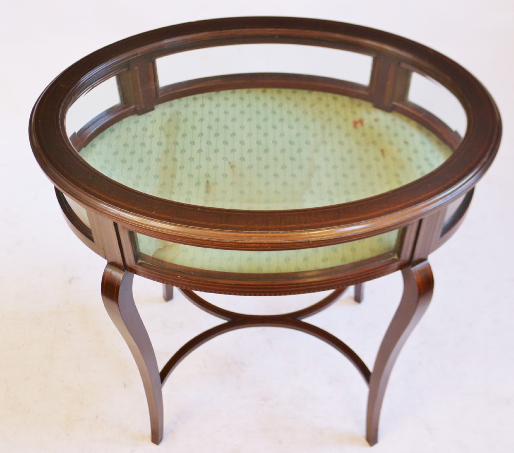 An Edwardian oval mahogany bijouterie table with glass top and sides, satinwood line inlay, curved legs, and an X-form stretcher. View III