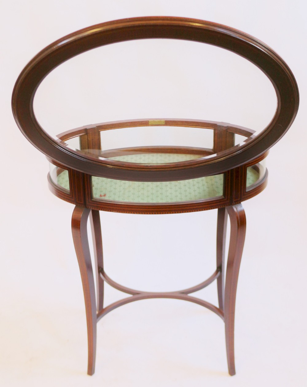 An Edwardian oval mahogany bijouterie table with glass top and sides, satinwood line inlay, curved legs, and an X-form stretcher. View V