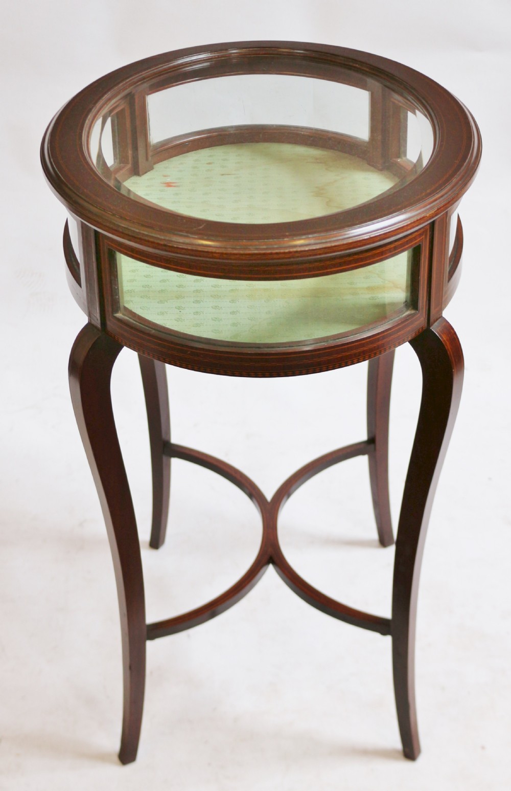 An Edwardian oval mahogany bijouterie table with glass top and sides, satinwood line inlay, curved legs, and an X-form stretcher. View VI