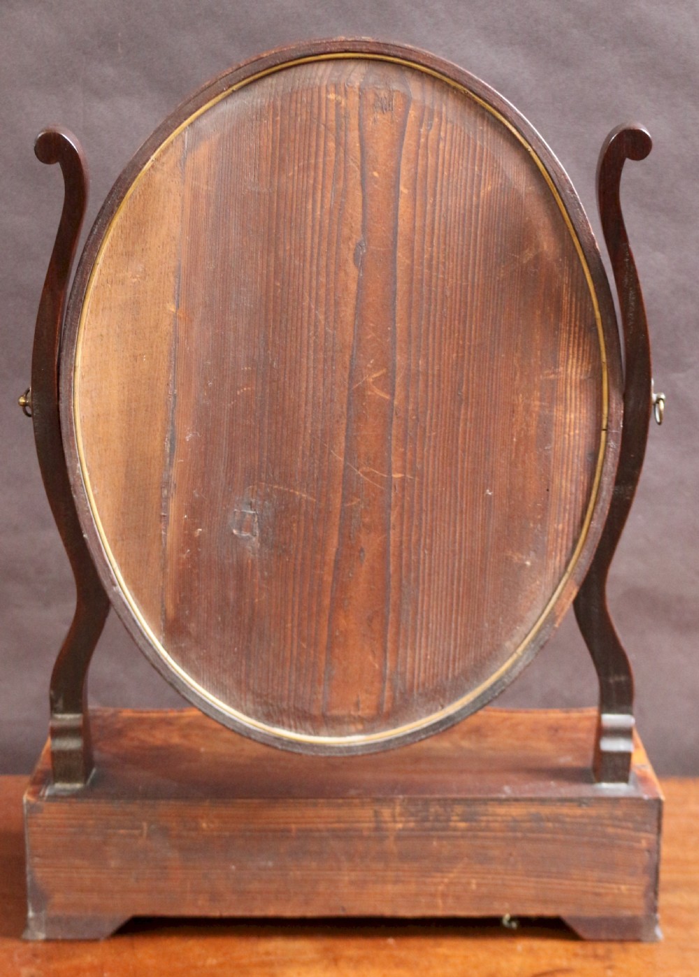 A George III mahogany toilet mirror featuring an oval adjustable mirror plate mounted on curved uprights above a serpentine base with three small drawers. View VI