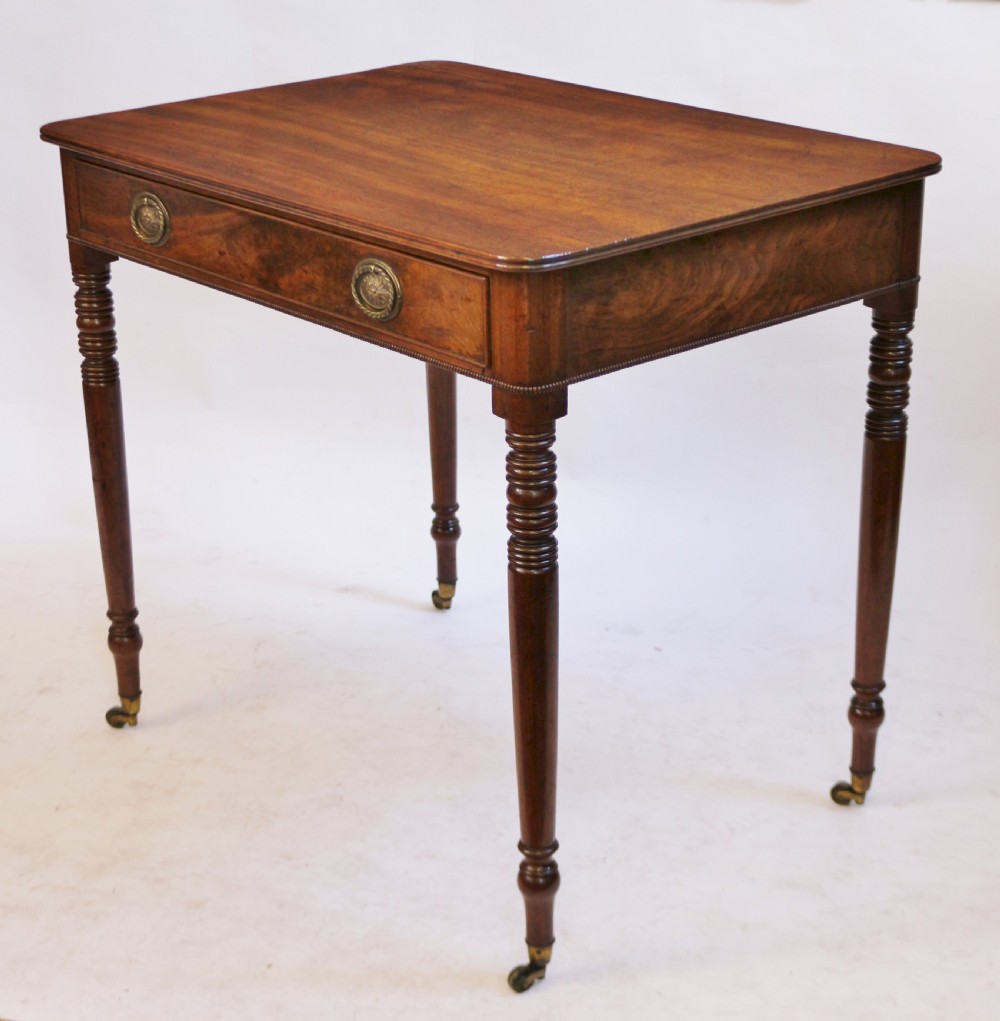 A George IV mahogany side table featuring a single frieze drawer with brass ring handles, turned legs, and brass castors. View II