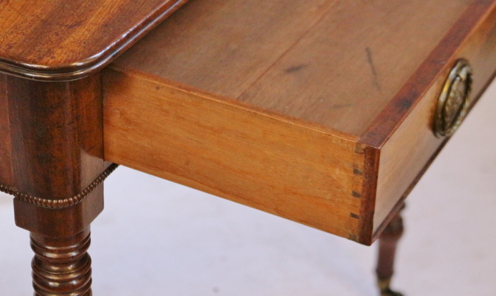 A George IV mahogany side table featuring a single frieze drawer with brass ring handles, turned legs, and brass castors. View IV