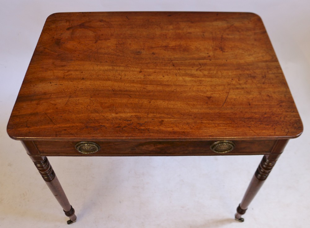 A George IV mahogany side table featuring a single frieze drawer with brass ring handles, turned legs, and brass castors. View V