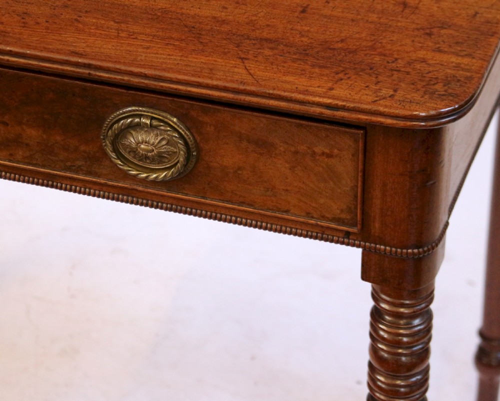 A George IV mahogany side table featuring a single frieze drawer with brass ring handles, turned legs, and brass castors. View VII