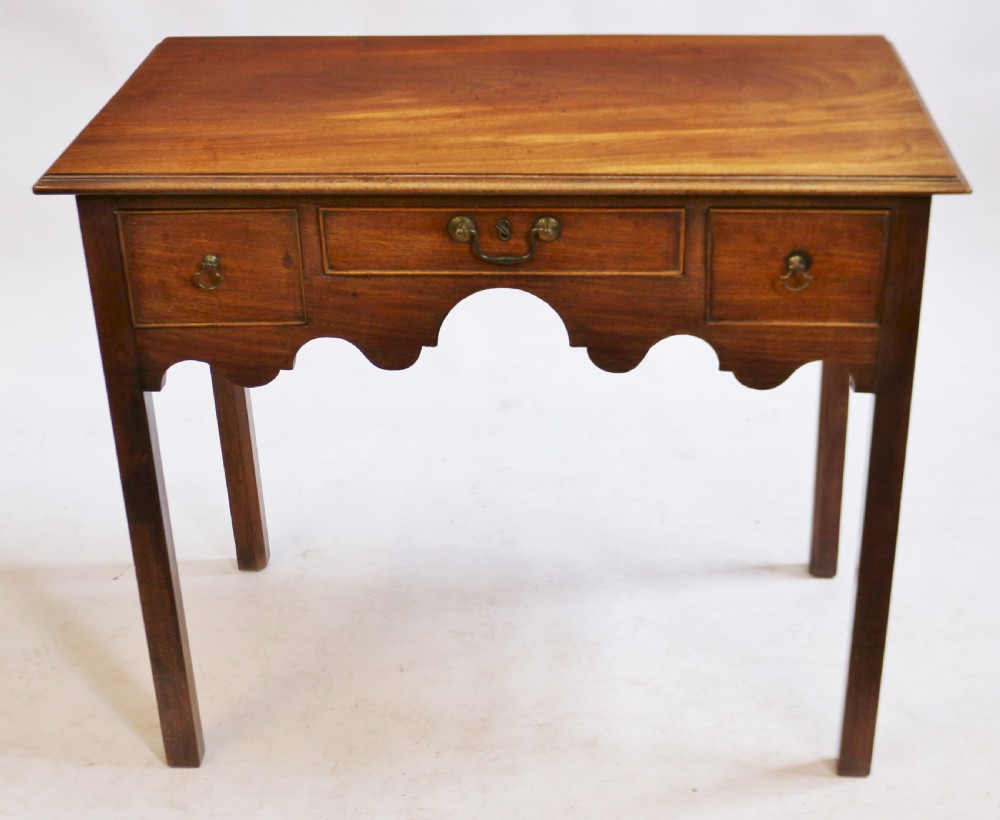 A George III mahogany lowboy table featuring a moulded top over three drawers with brass handles and a scalloped apron on square legs.