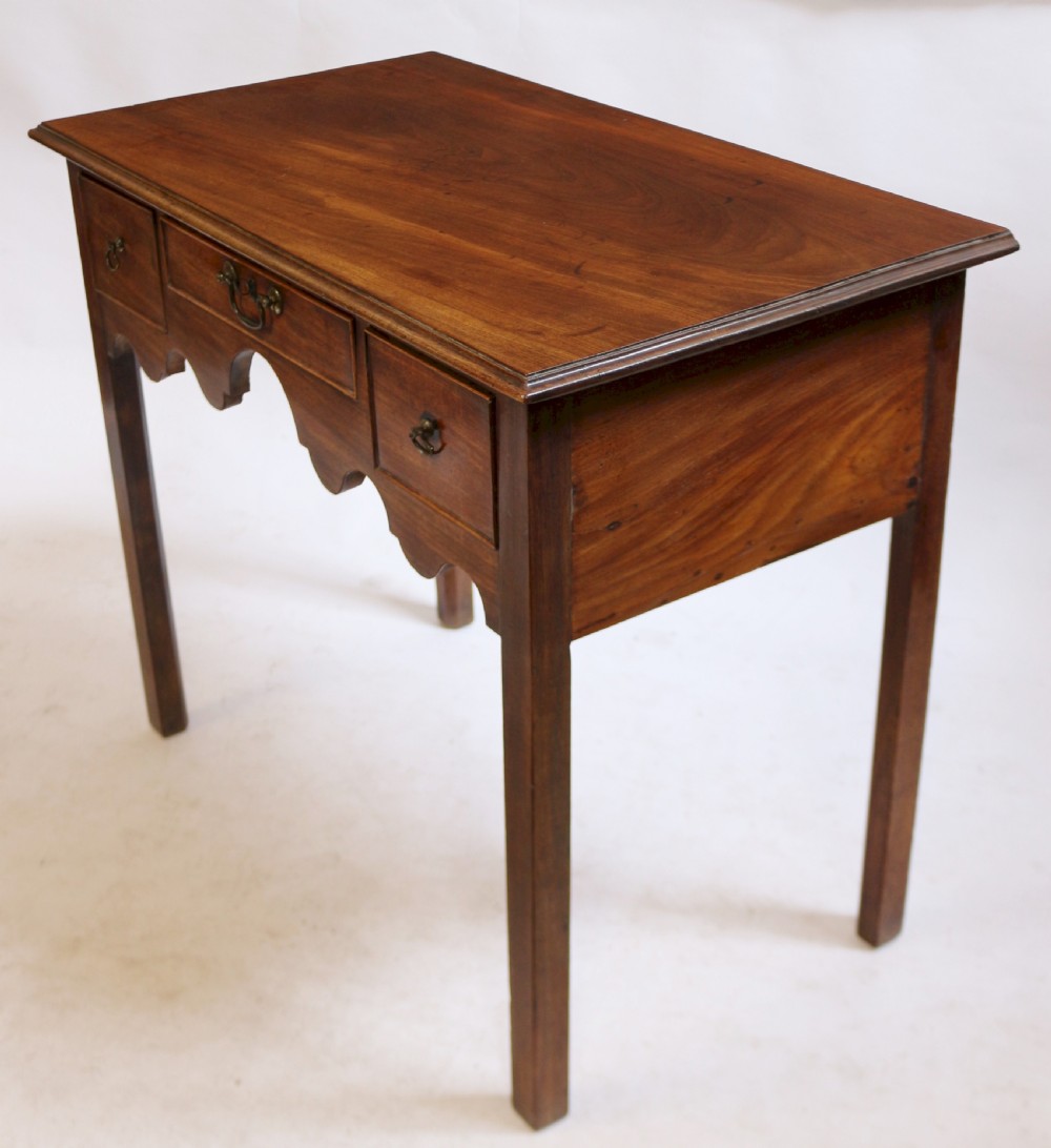 A George III mahogany lowboy table featuring a moulded top over three drawers with brass handles and a scalloped apron on square legs. View III
