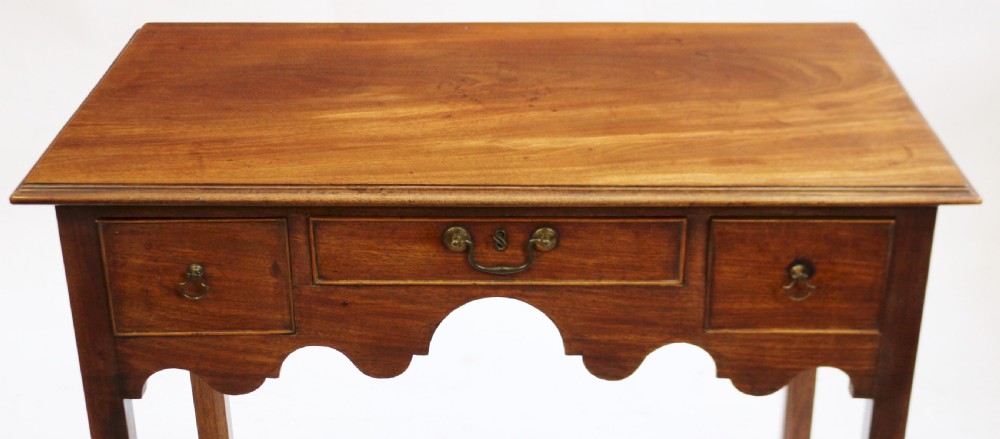 A George III mahogany lowboy table featuring a moulded top over three drawers with brass handles and a scalloped apron on square legs. View V