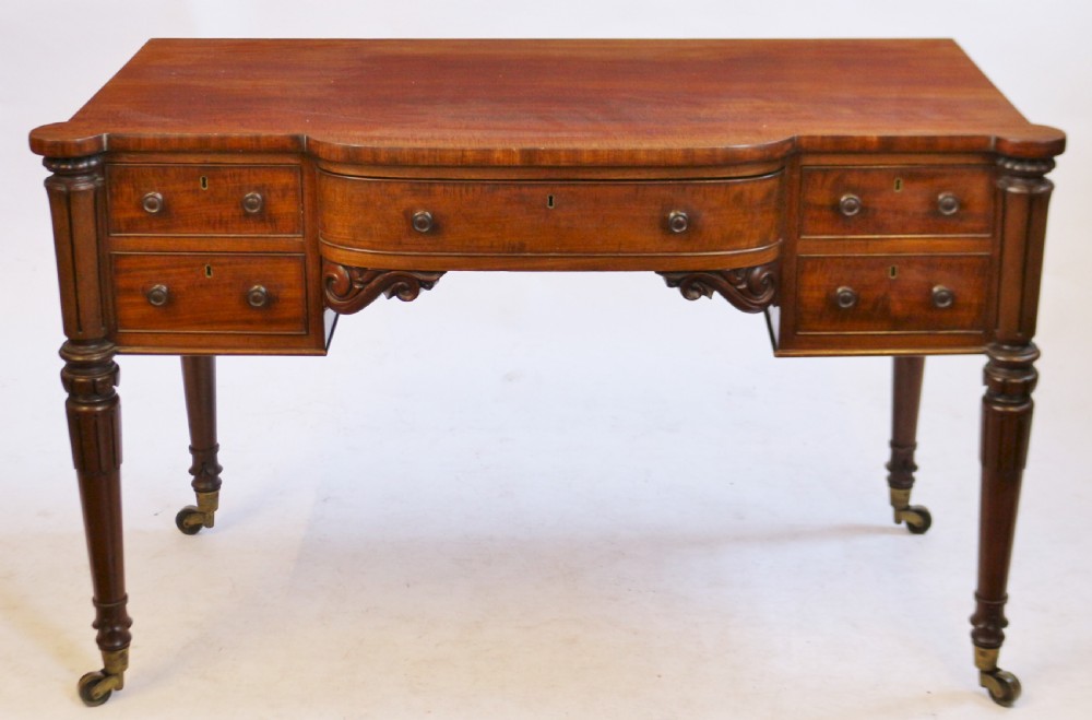 An early Victorian mahogany kneehole desk with five drawers, turned legs on brass castors, and carved corner spandrels.