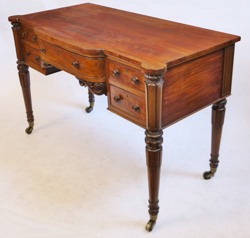 An early Victorian mahogany kneehole desk with five drawers, turned legs on brass castors, and carved corner spandrels. View II