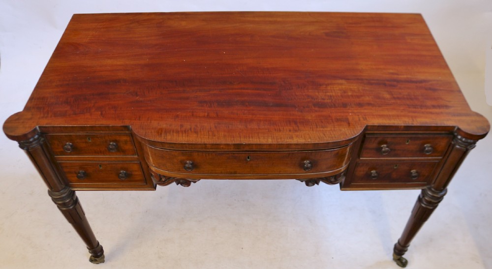 An early Victorian mahogany kneehole desk with five drawers, turned legs on brass castors, and carved corner spandrels. View IV