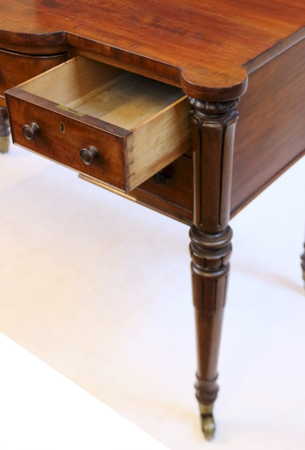 An early Victorian mahogany kneehole desk with five drawers, turned legs on brass castors, and carved corner spandrels. View V