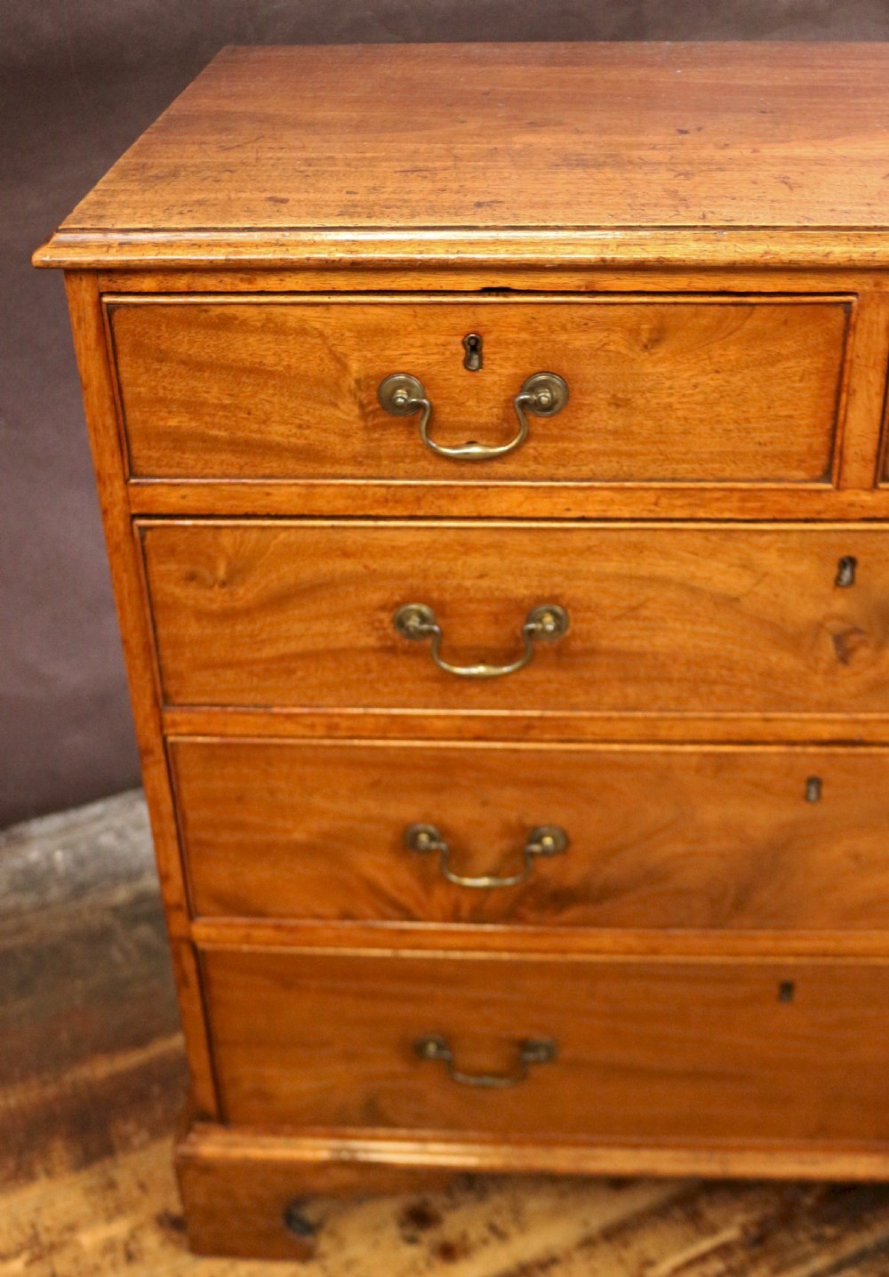 A George III mahogany chest of drawers featuring two short drawers over three long drawers with brass swan-neck handles and bracket feet. View VI
