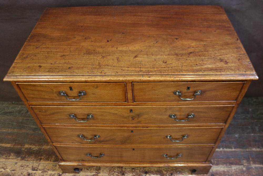 A George III mahogany chest of drawers featuring two short drawers over three long drawers with brass swan-neck handles and bracket feet. View VII