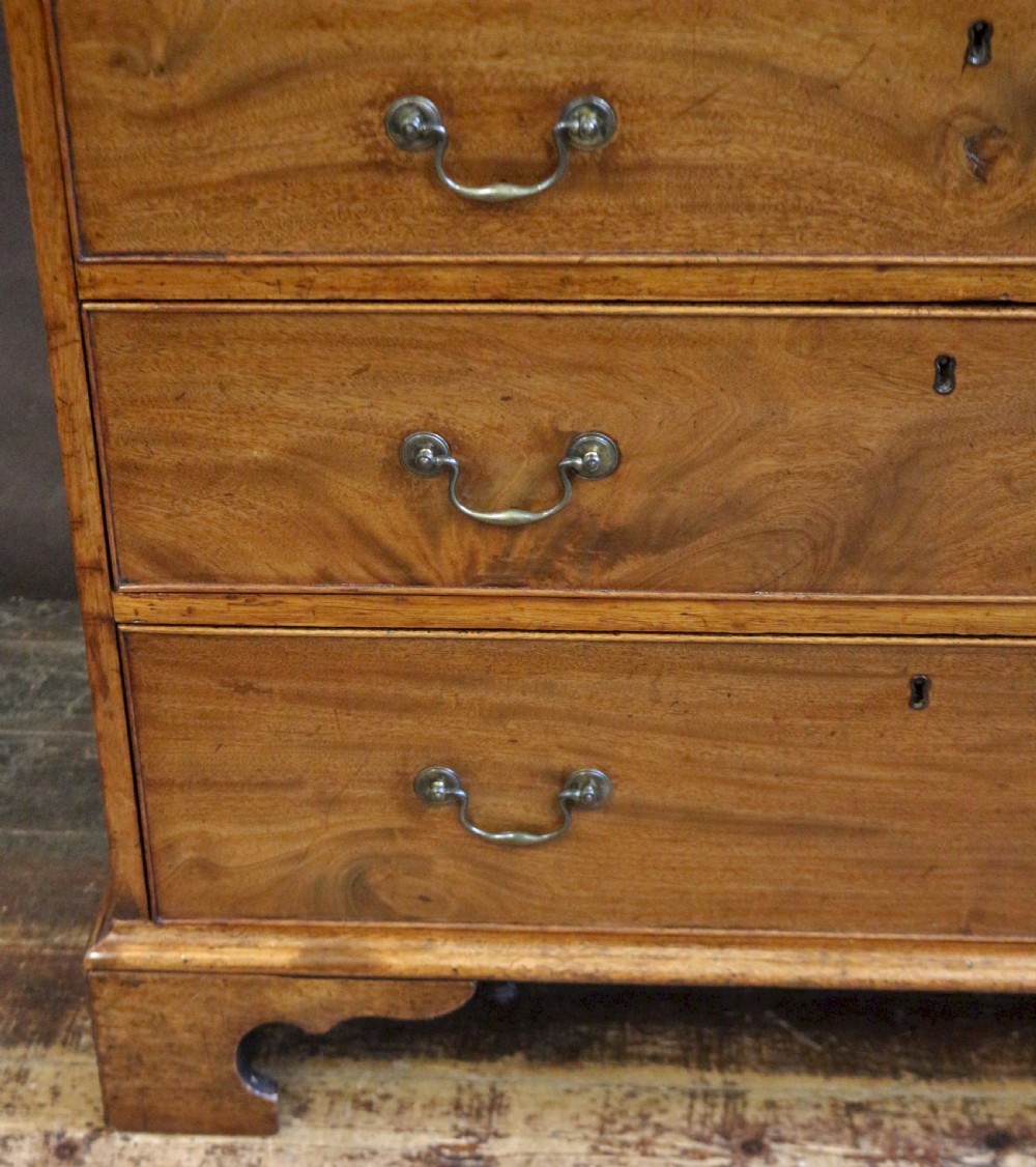 A George III mahogany chest of drawers featuring two short drawers over three long drawers with brass swan-neck handles and bracket feet. View VIII