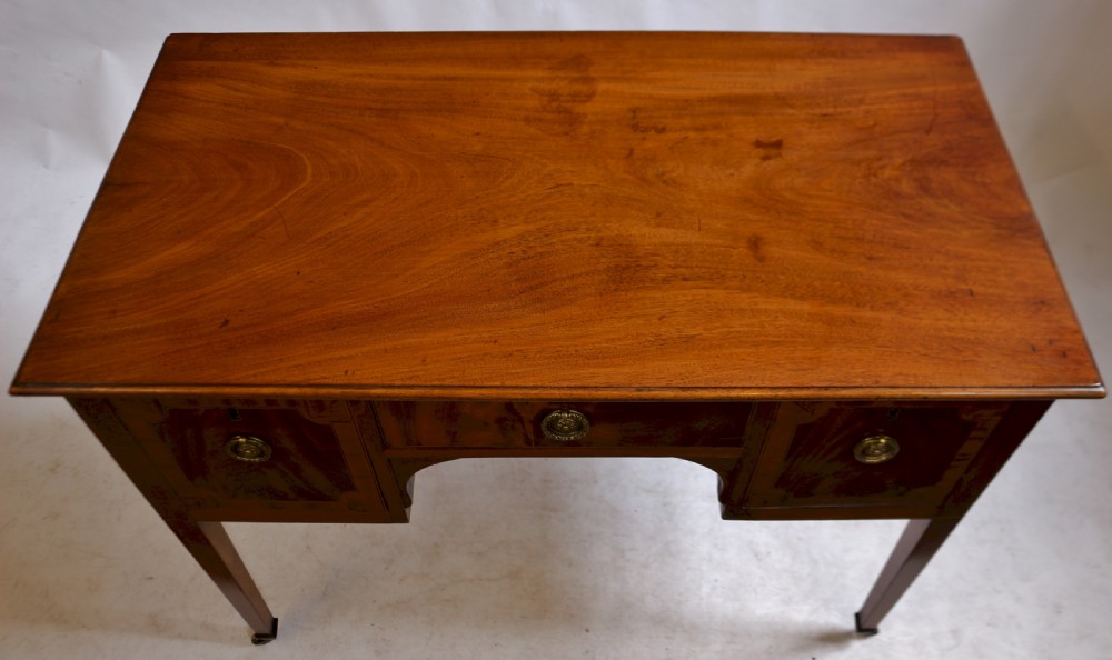 A George III mahogany kneehole desk featuring three inlaid drawers, central kneehole arch, brass handles, and square tapered legs with brass castors. View II