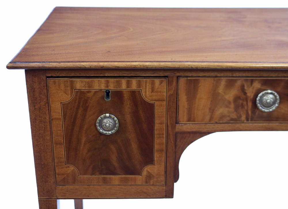 A George III mahogany kneehole desk featuring three inlaid drawers, central kneehole arch, brass handles, and square tapered legs with brass castors. View VI