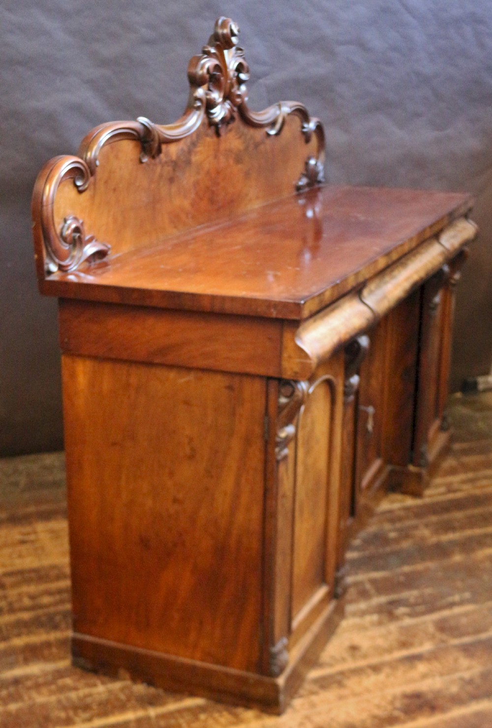 A Victorian mahogany four-door sideboard featuring a scroll-carved backboard, flame mahogany doors, and a solid plinth base. View III