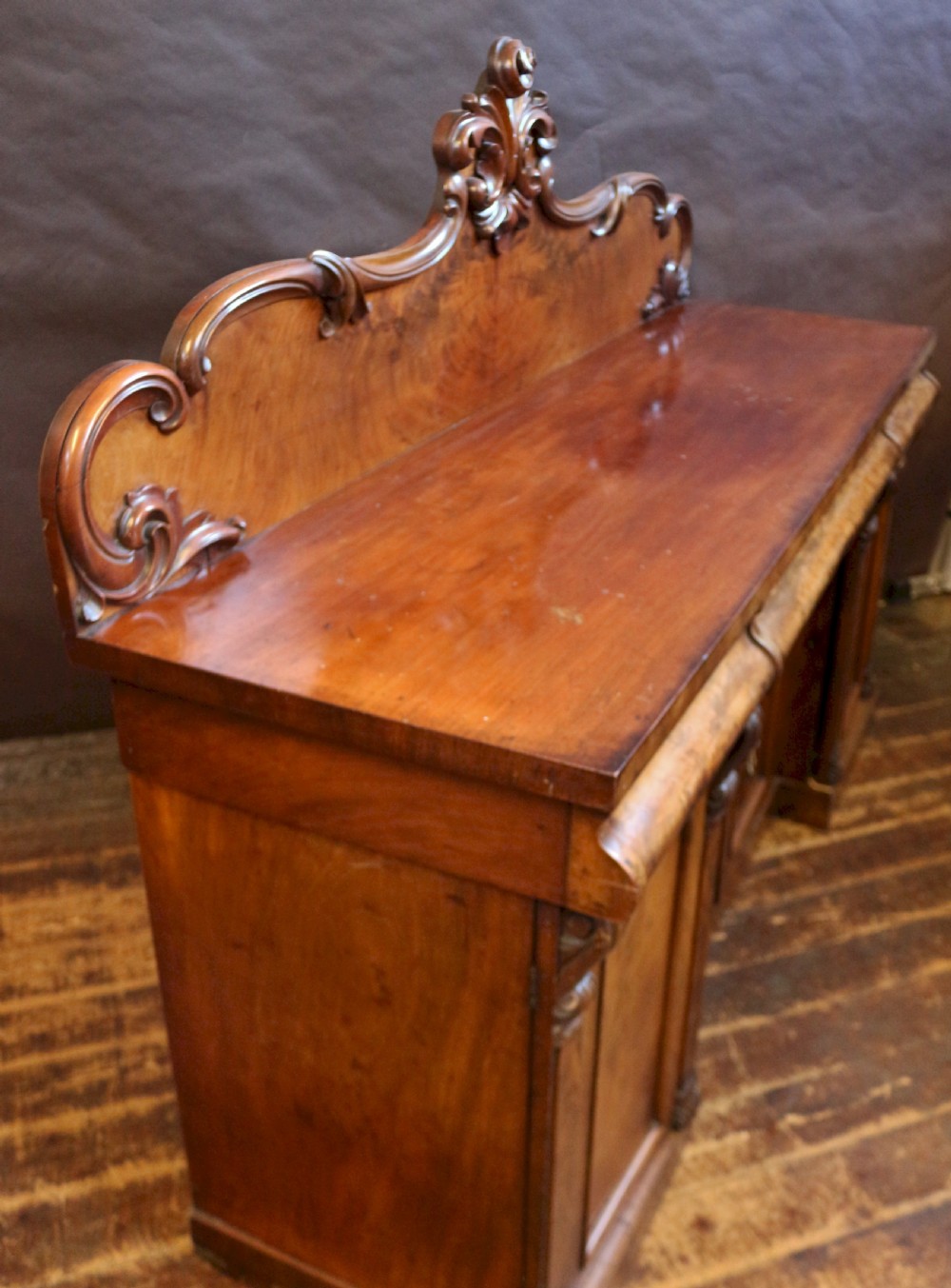 A Victorian mahogany four-door sideboard featuring a scroll-carved backboard, flame mahogany doors, and a solid plinth base. View IV