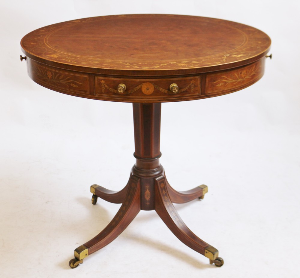 An Edwardian mahogany circular drum table featuring floral and zodiac marquetry inlays, a frieze drawer with dual brass knobs, and a central pedestal resting on four splayed legs with brass castors.