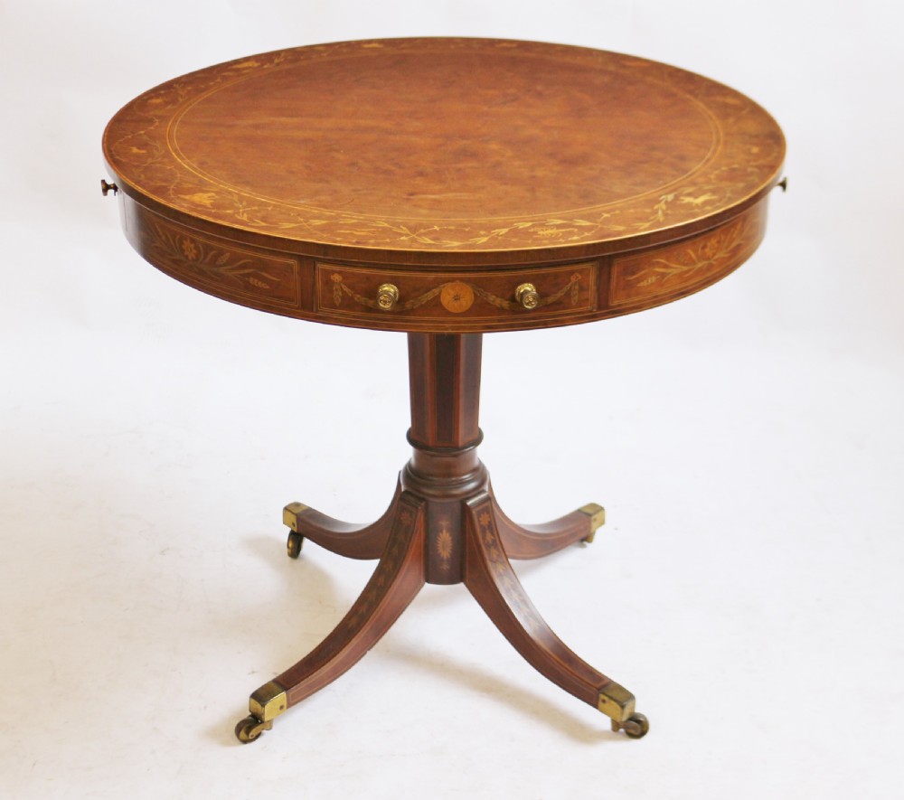 An Edwardian mahogany circular drum table featuring floral and zodiac marquetry inlays, a frieze drawer with dual brass knobs, and a central pedestal resting on four splayed legs with brass castors. View II