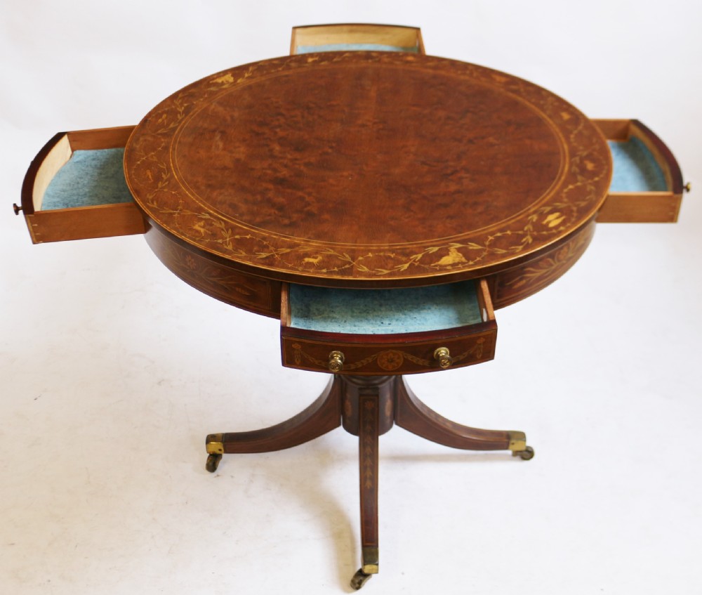 An Edwardian mahogany circular drum table featuring floral and zodiac marquetry inlays, a frieze drawer with dual brass knobs, and a central pedestal resting on four splayed legs with brass castors. View IV