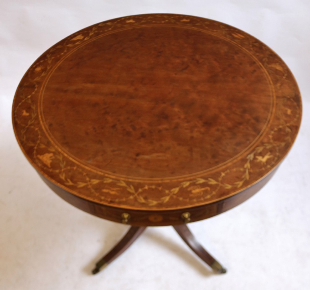 An Edwardian mahogany circular drum table featuring floral and zodiac marquetry inlays, a frieze drawer with dual brass knobs, and a central pedestal resting on four splayed legs with brass castors. View V