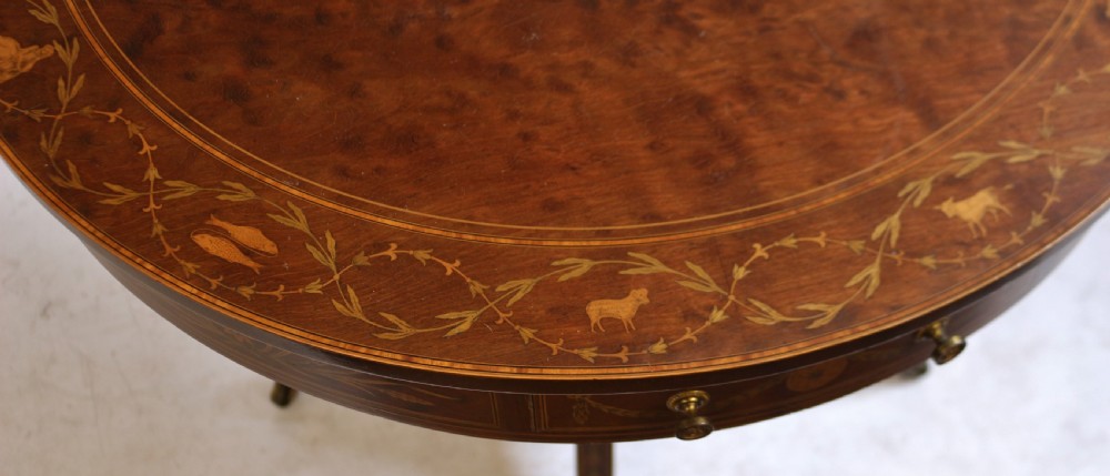 An Edwardian mahogany circular drum table featuring floral and zodiac marquetry inlays, a frieze drawer with dual brass knobs, and a central pedestal resting on four splayed legs with brass castors. View VIII