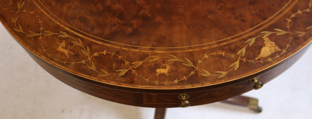 An Edwardian mahogany circular drum table featuring floral and zodiac marquetry inlays, a frieze drawer with dual brass knobs, and a central pedestal resting on four splayed legs with brass castors. View IX