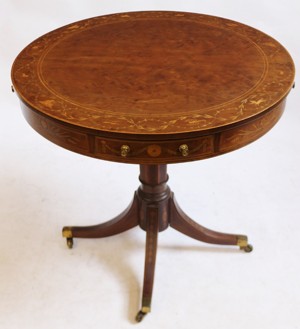An Edwardian mahogany circular drum table featuring floral and zodiac marquetry inlays, a frieze drawer with dual brass knobs, and a central pedestal resting on four splayed legs with brass castors. View X