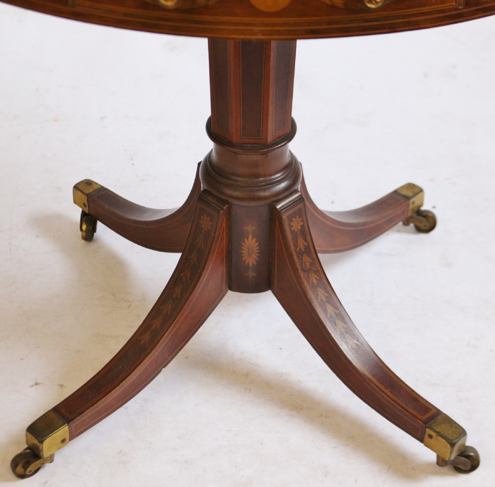 An Edwardian mahogany circular drum table featuring floral and zodiac marquetry inlays, a frieze drawer with dual brass knobs, and a central pedestal resting on four splayed legs with brass castors. View XI