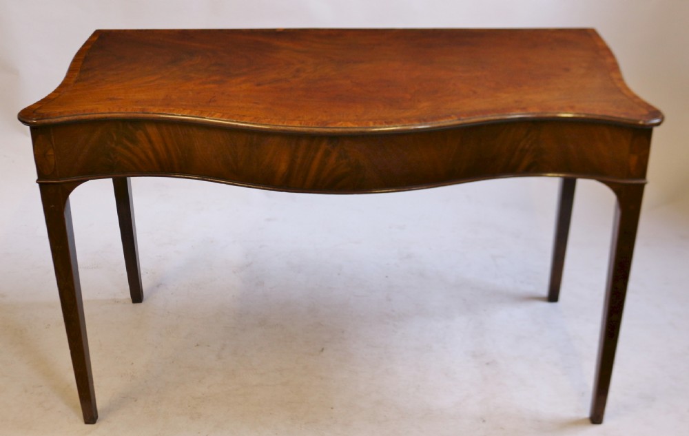 A George III mahogany serving table with a wavy serpentine front, flame mahogany veneer, and four tapered square legs.