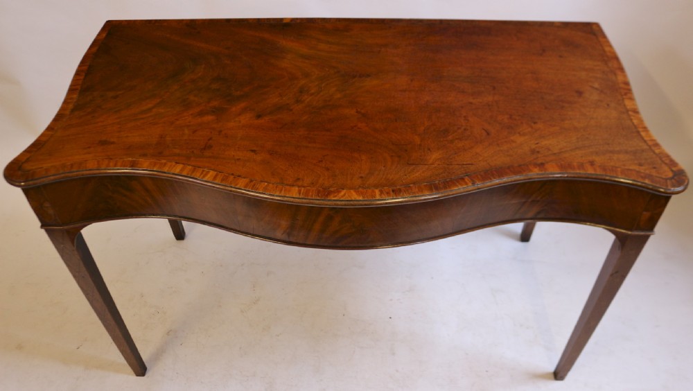 A George III mahogany serving table with a wavy serpentine front, flame mahogany veneer, and four tapered square legs. View II