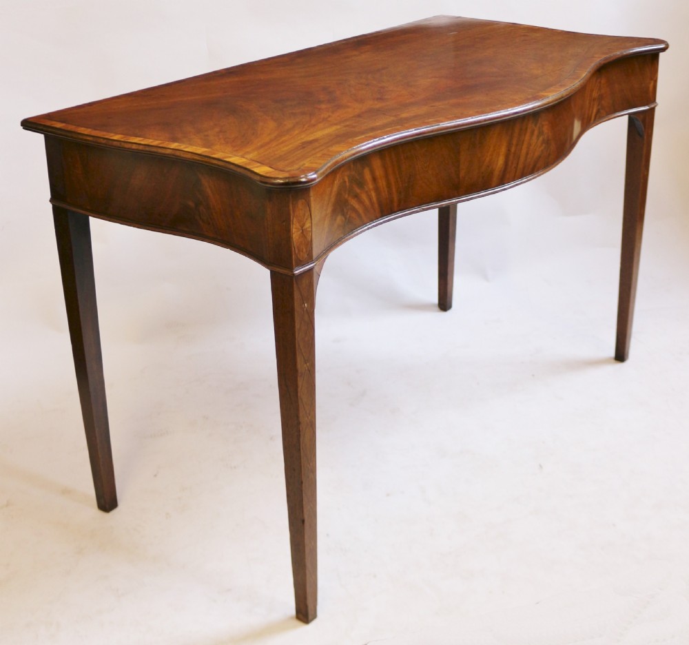 A George III mahogany serving table with a wavy serpentine front, flame mahogany veneer, and four tapered square legs. View III